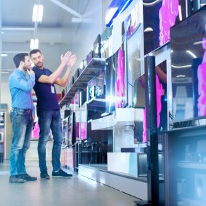 In the Electronics Store Professional Consultant Shows Latest 4K In the Electronics Store Professional Consultant Shows Latest 4K UHD TV's to a Young Man, They Talk about Specifications and What Model is Best for Young Man's Home. Store is Bright, Modern and Has all the Latest Models.